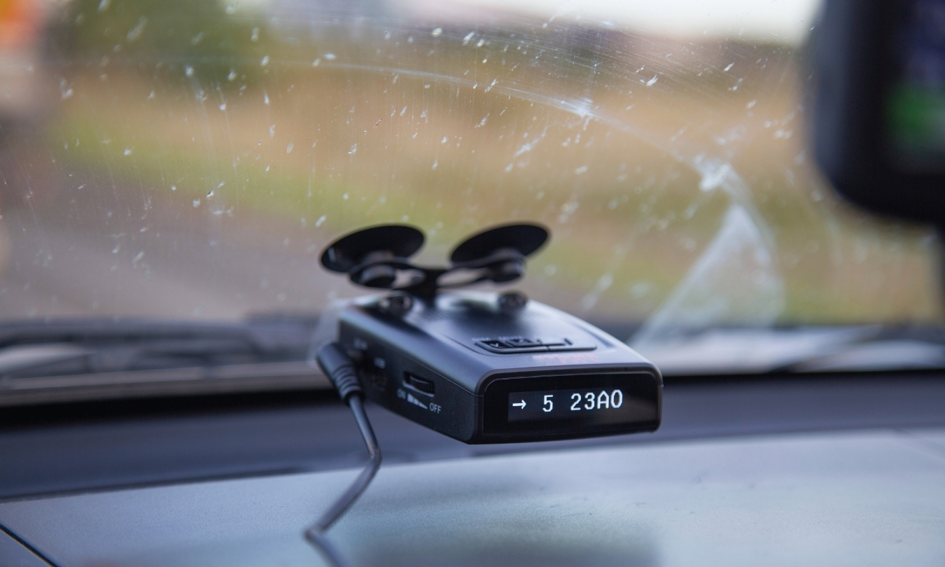 Black radar detector attached to car windshield with suction cups